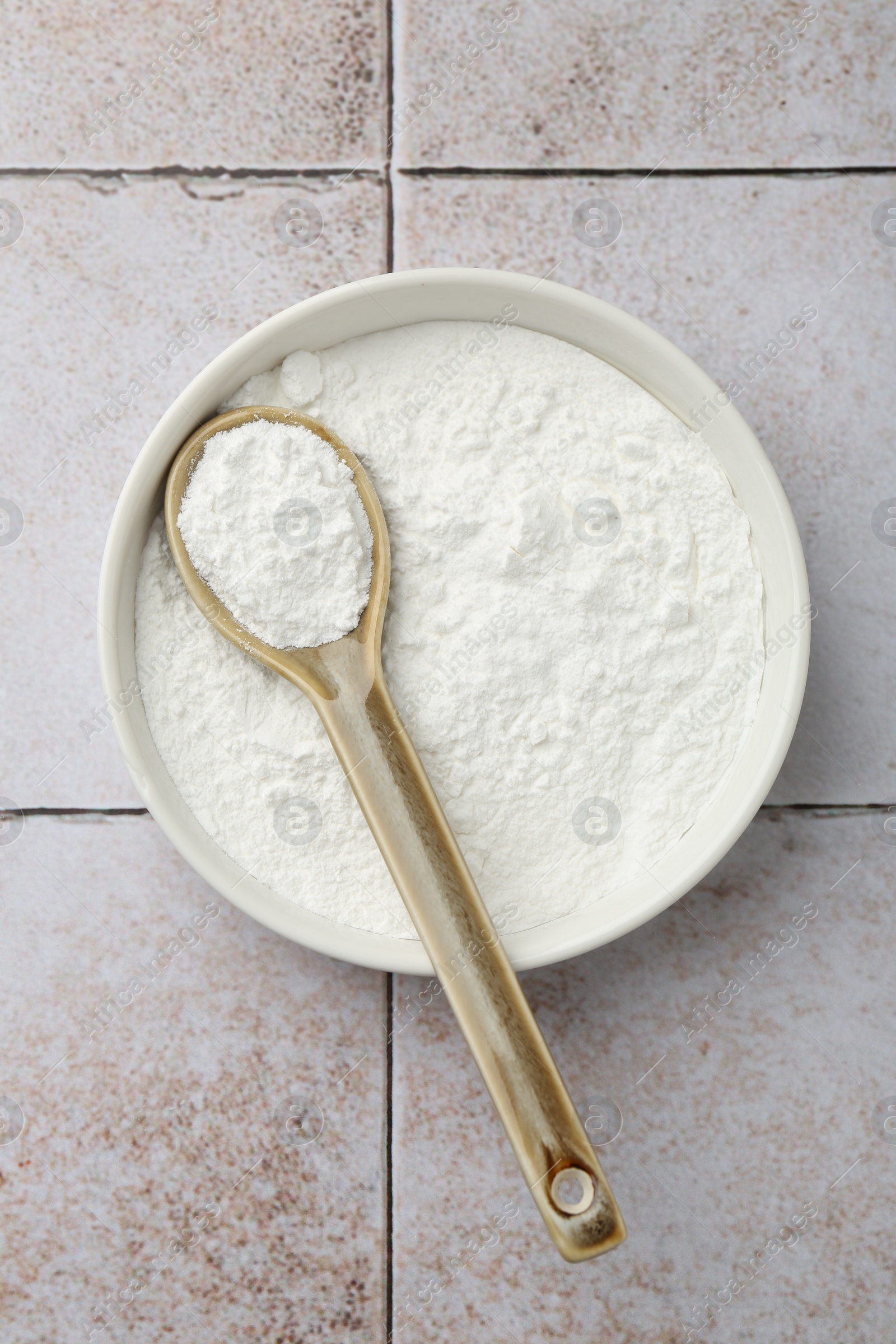 Photo of Baking powder in bowl and spoon on light tiled table, top view