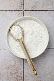 Photo of Baking powder in bowl and spoon on light tiled table, top view