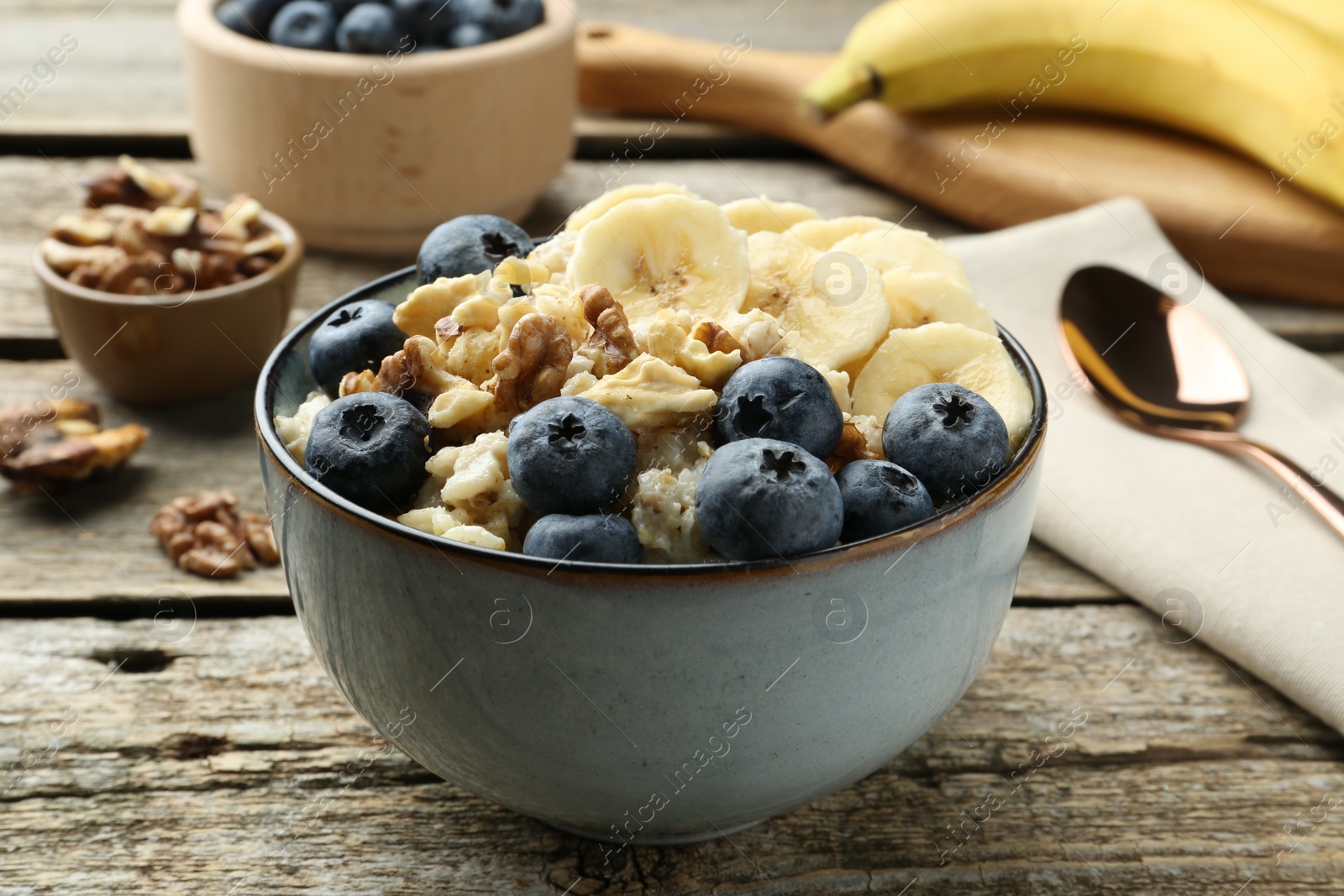 Photo of Tasty oatmeal with banana, blueberries and walnuts served in bowl on wooden table