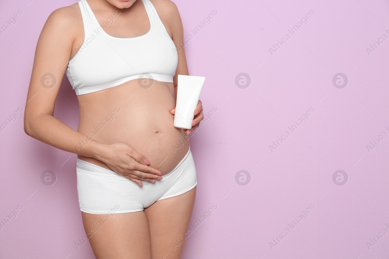 Photo of Pregnant woman holding body cream on color background, closeup with space for text