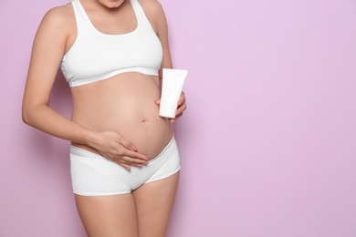 Photo of Pregnant woman holding body cream on color background, closeup with space for text