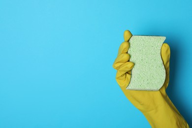 Photo of Woman in rubber glove holding sponge on light blue background, top view. Space for text