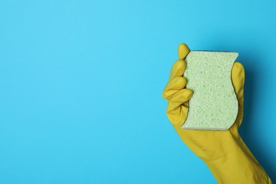 Woman in rubber glove holding sponge on light blue background, top view. Space for text