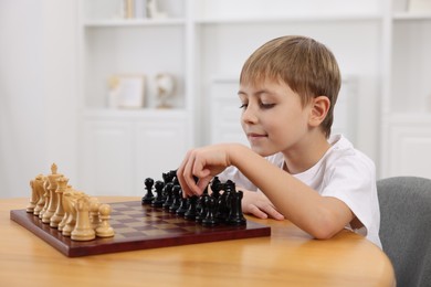 Cute little boy playing chess at table in room