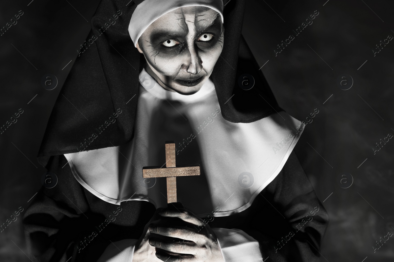 Photo of Scary devilish nun with cross on black background. Halloween party look