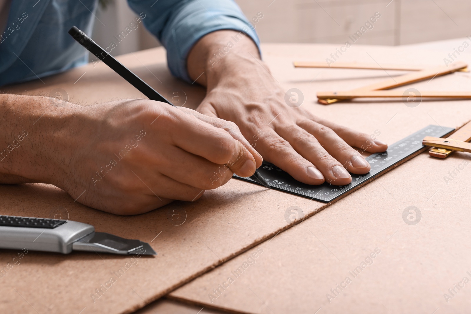 Photo of Man with pencil, utility knife and ruler at table indoors, closeup