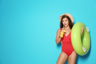 Beautiful young woman with inflatable ring and glass of cocktail on color background