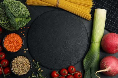 Slate plate surrounded by different ingredients on black table, flat lay with space for text. Cooking classes