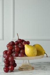 Dessert stand with fresh ripe pears and grapes on white marble table, space for text