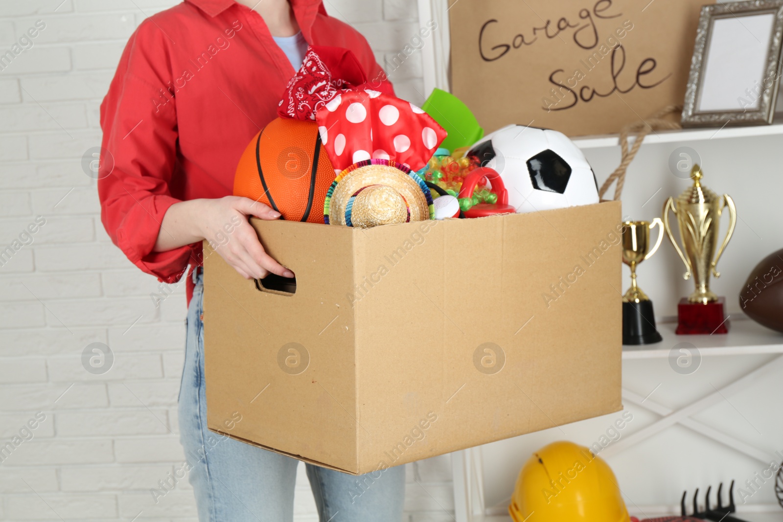 Photo of Woman holding box of unwanted stuff indoors, closeup