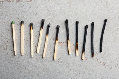 Photo of Row of burnt matches and whole one on grey background, flat lay. Uniqueness concept