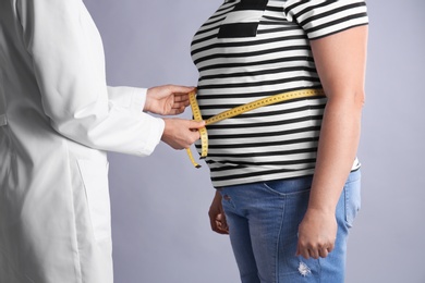 Photo of Doctor measuring fat woman's waist on grey background. Weight loss