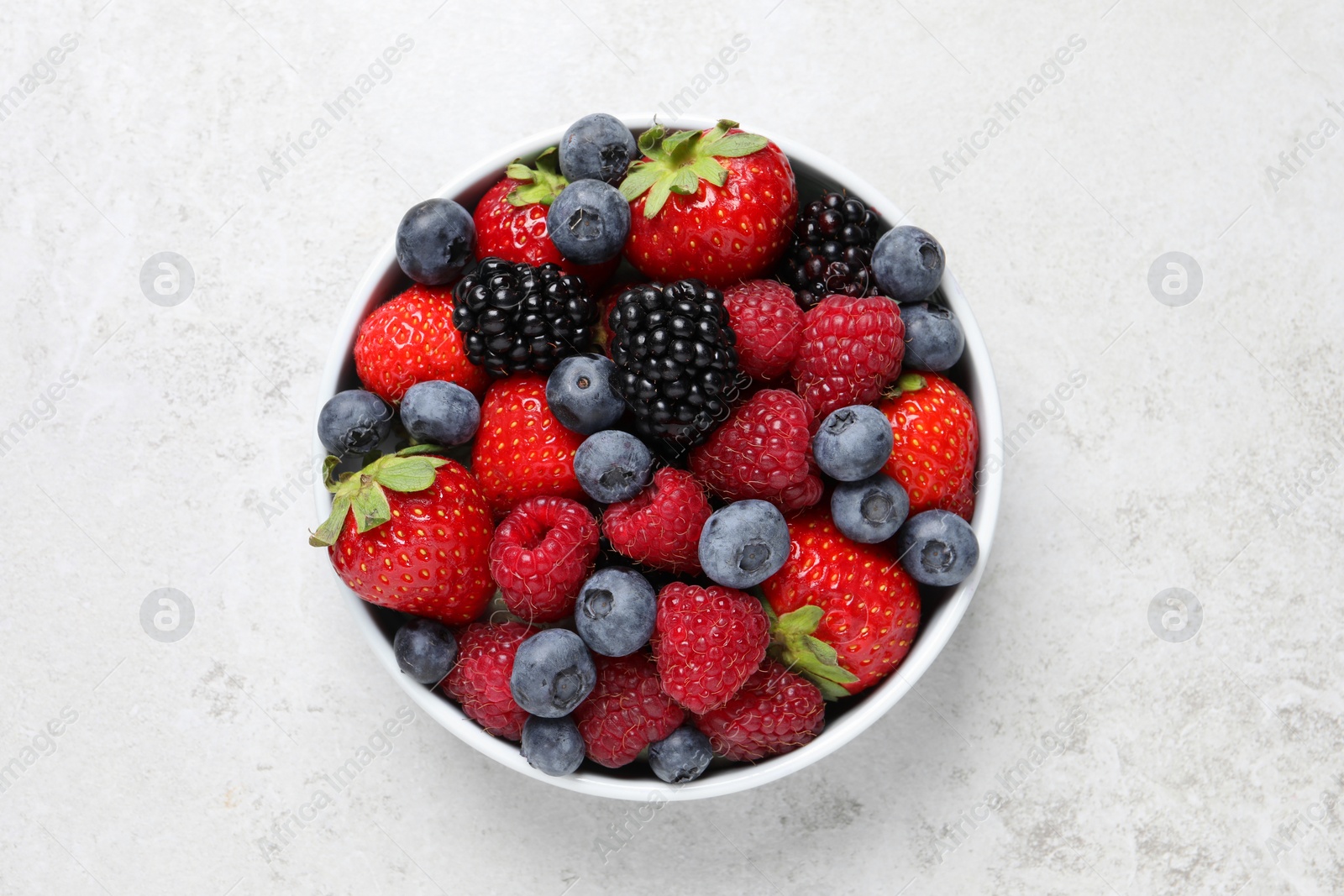 Photo of Many different fresh ripe berries in bowl on light grey table, top view