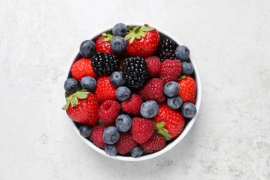 Many different fresh ripe berries in bowl on light grey table, top view