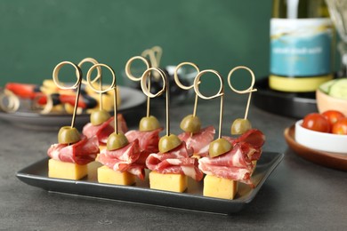 Tasty canapes with olives, prosciutto and cheese on grey table, closeup