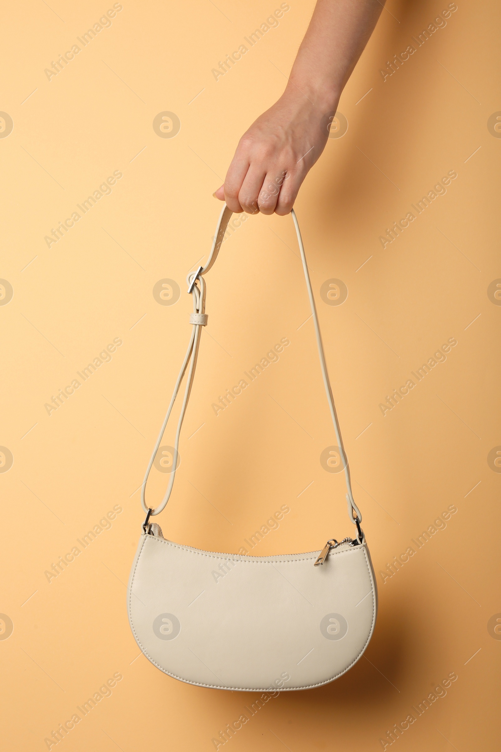 Photo of Woman holding stylish beige bag on pale orange background, closeup