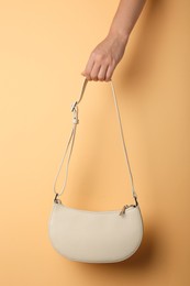 Woman holding stylish beige bag on pale orange background, closeup