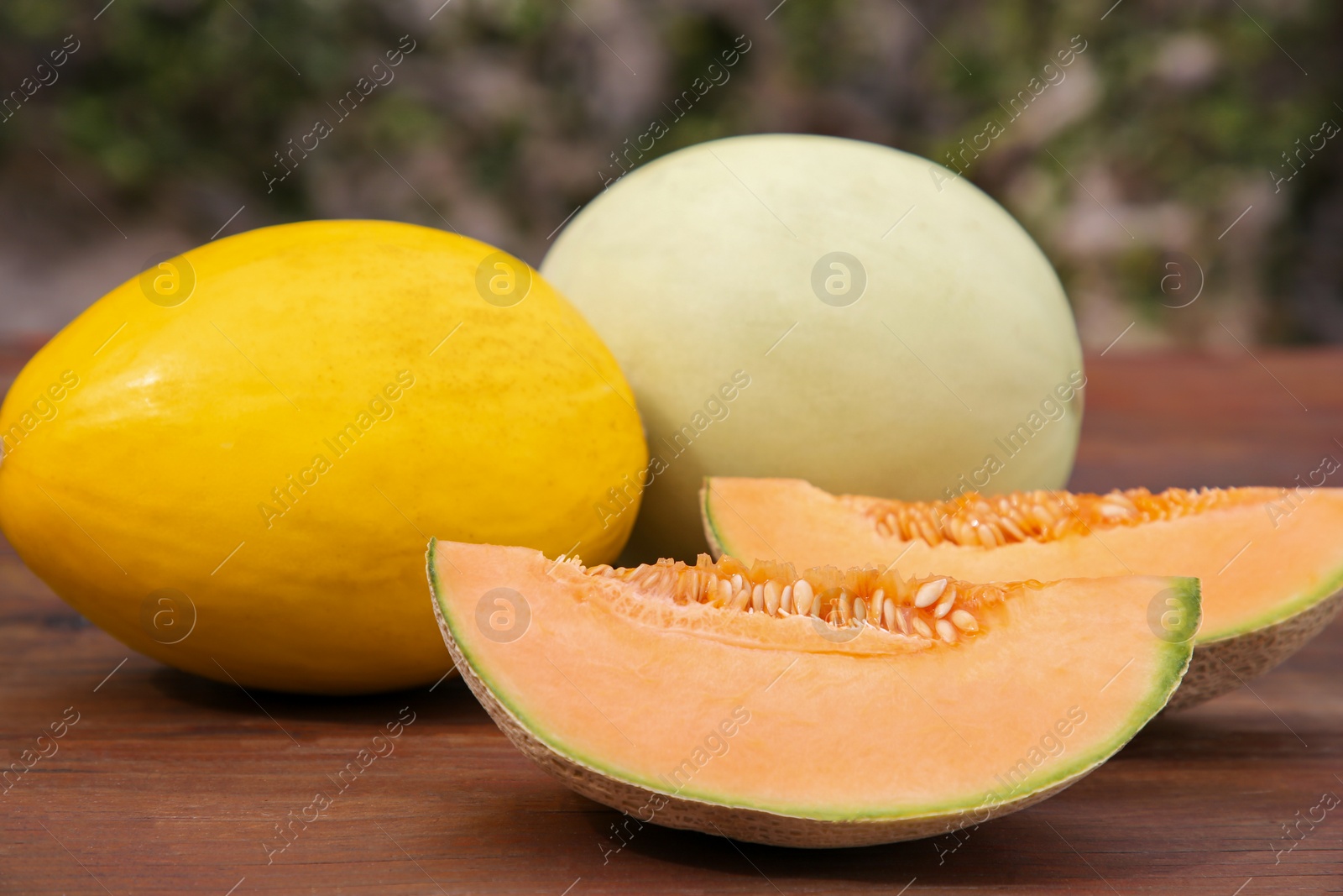 Photo of Whole and cut ripe melons on wooden table outdoors