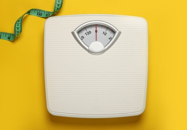 Photo of Weigh scales and measuring tape on yellow background, top view. Overweight concept