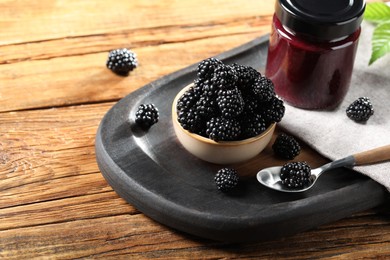 Photo of Fresh ripe blackberries and tasty jam on wooden table. Space for text