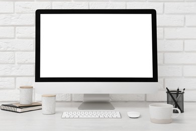 Photo of Office workplace with computer, cup and stationery on light table near white brick wall