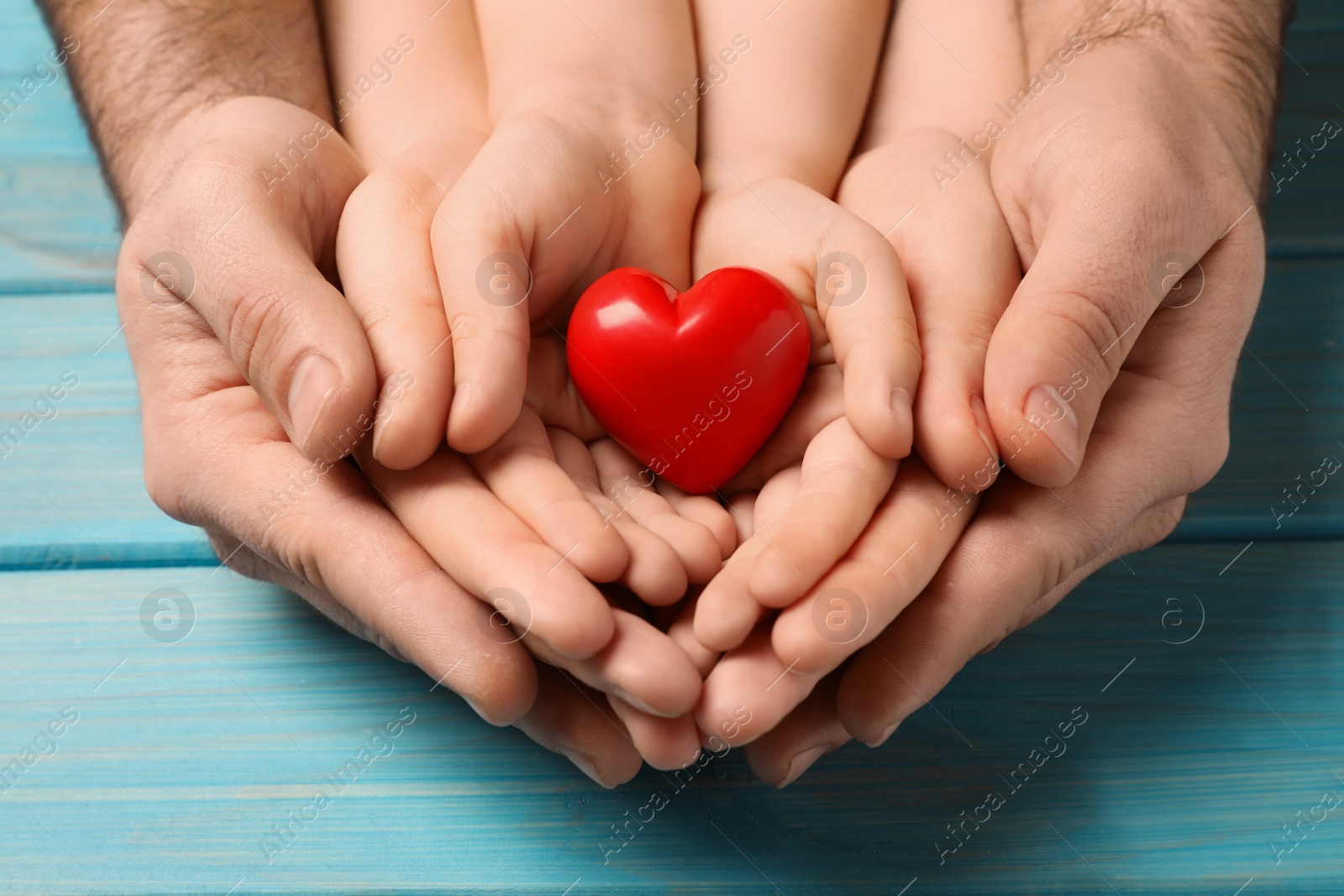 Photo of Parents and kid holding red heart in hands at light blue wooden table, closeup