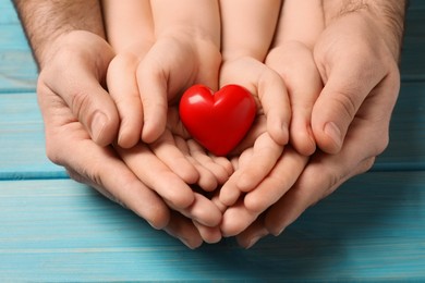 Photo of Parents and kid holding red heart in hands at light blue wooden table, closeup