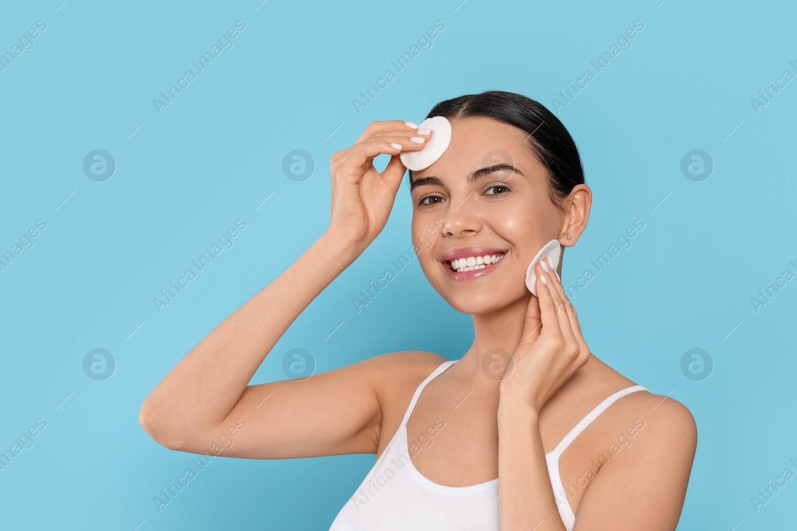 Photo of Young woman using cotton pads with micellar water on light blue background