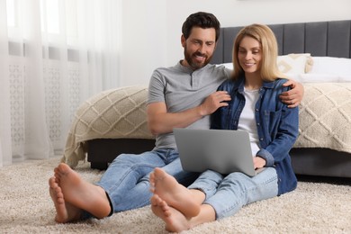 Happy couple with laptop on floor in bedroom