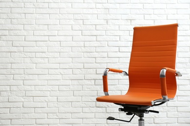 Comfortable office chair near white brick wall. Space for text