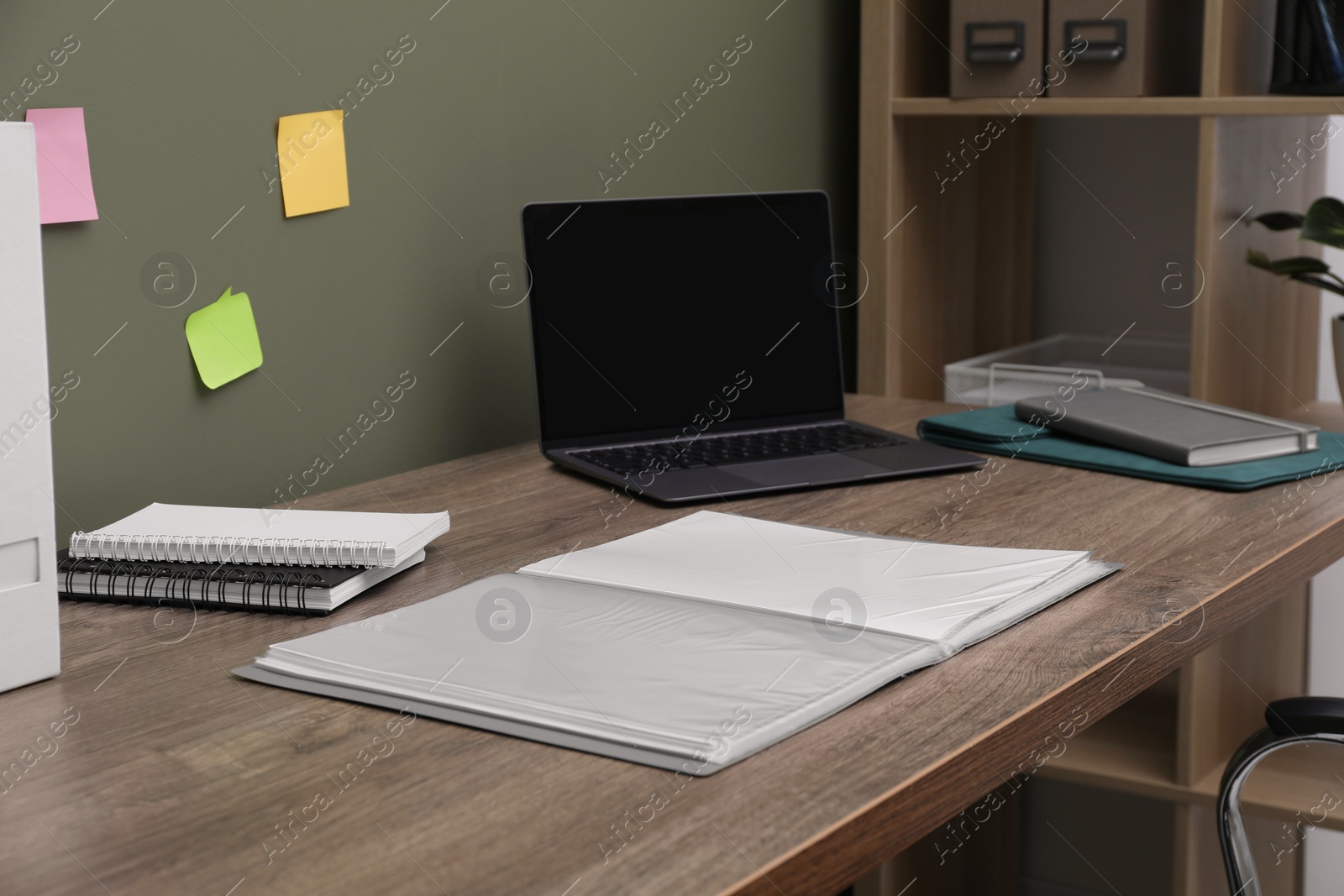 Photo of Folder with punched pockets and laptop on wooden table in office