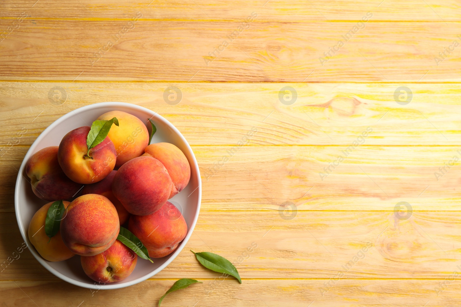 Photo of Fresh sweet peaches in bowl on wooden table. Space for text