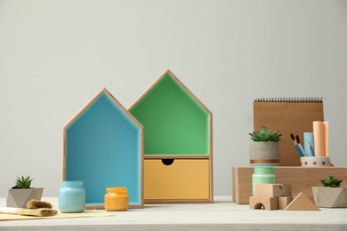 Composition with house shaped shelves and jars of paints on white table. Interior elements