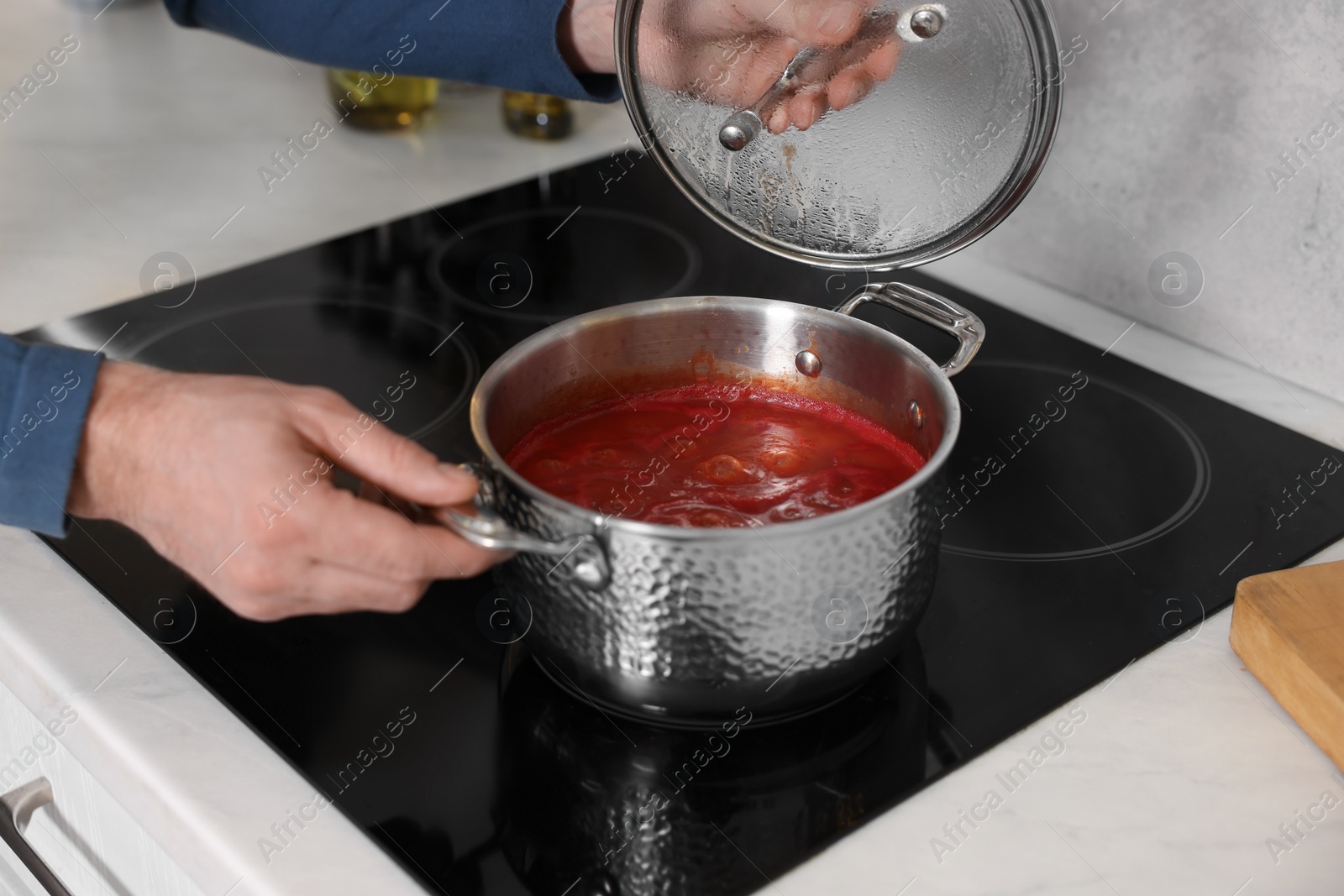 Photo of Man cooking tomato soup on cooktop in kitchen, closeup