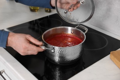 Man cooking tomato soup on cooktop in kitchen, closeup