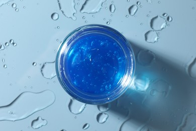 Photo of Open jar of cosmetic product and water drops on light blue background, top view