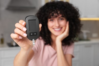 Photo of Diabetes. Happy woman holding digital glucometer in kitchen, selective focus