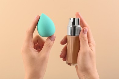 Photo of Woman with makeup sponge and skin foundation on beige background, closeup