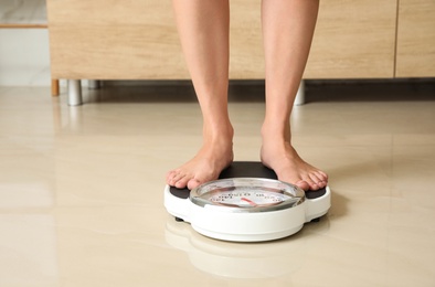 Photo of Woman standing on scales in bathroom. Overweight problem