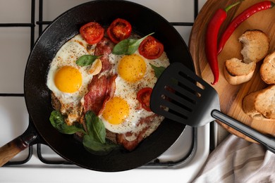 Delicious fried eggs with bacon and tomatoes in pan on stove, top view