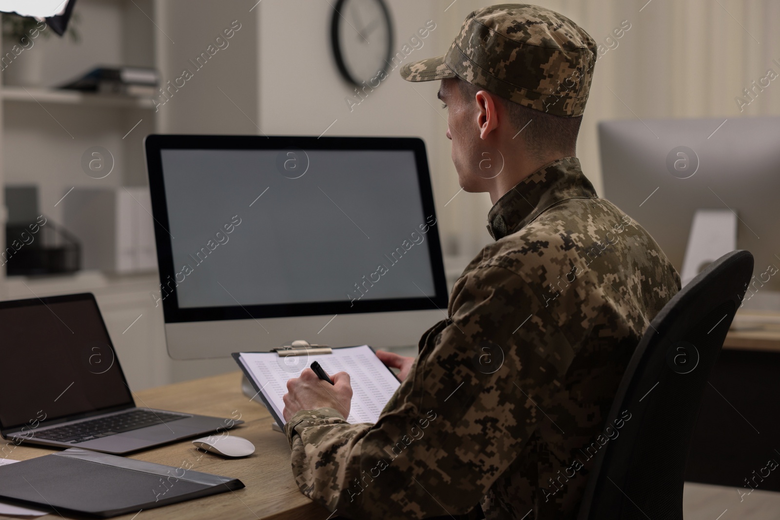 Photo of Military service. Soldier with clipboard working at table in office