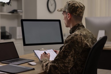 Photo of Military service. Soldier with clipboard working at table in office