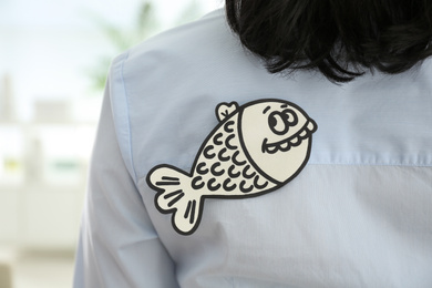 Woman with paper fish on back indoors, closeup. April fool's day