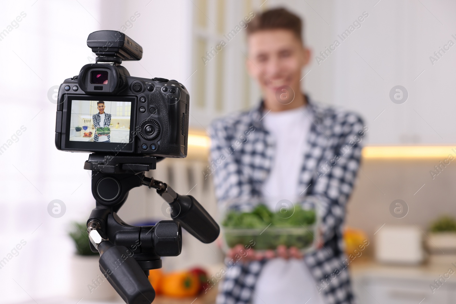 Photo of Food blogger recording video in kitchen, focus on camera