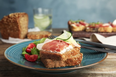 Photo of Plate of delicious bruschettas with prosciutto on wooden table