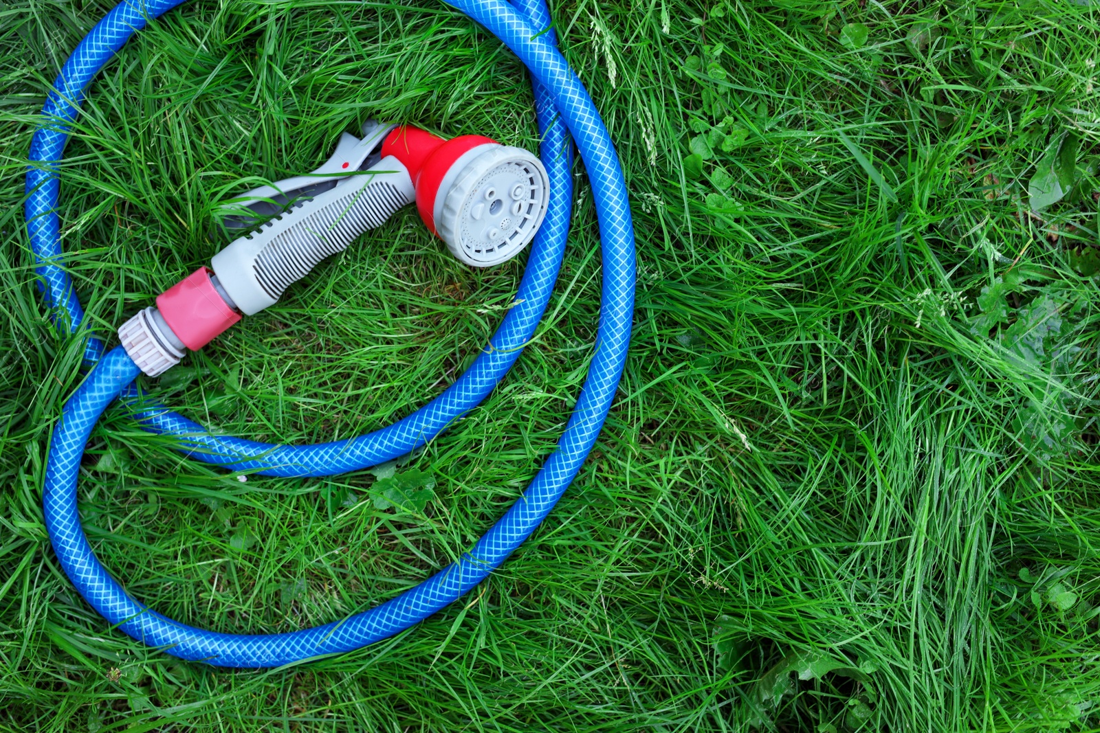 Photo of Watering hose with sprinkler on green grass outdoors, top view. Space for text