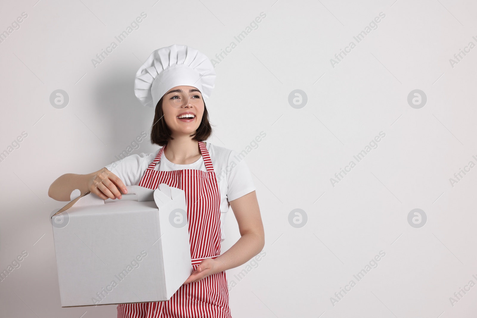 Photo of Happy confectioner with cake box on light grey background, space for text