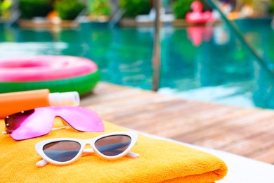 Beach towel and sunglasses on sun lounger near outdoor swimming pool at luxury resort. Space for text