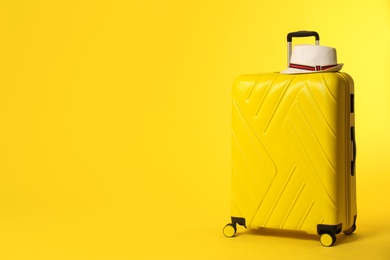 Photo of Bright suitcase with hat on color background. Space for text