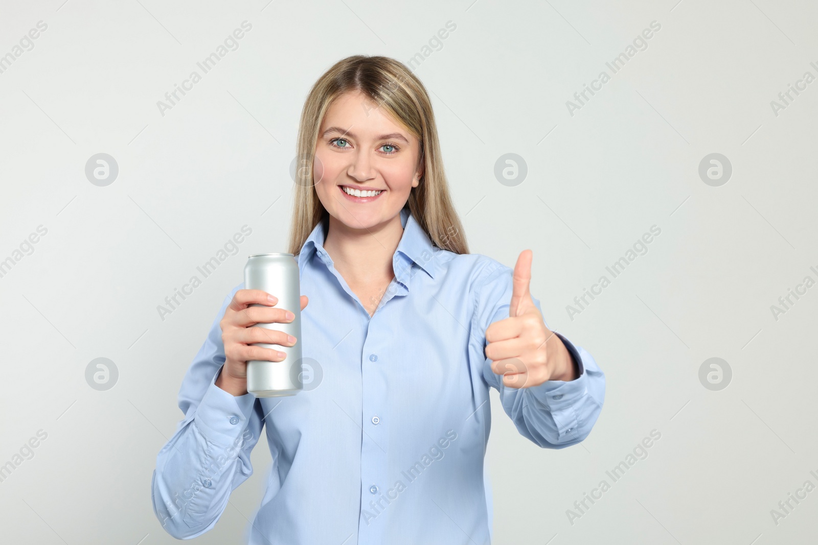 Photo of Beautiful happy woman holding beverage can and showing thumbs up on light background